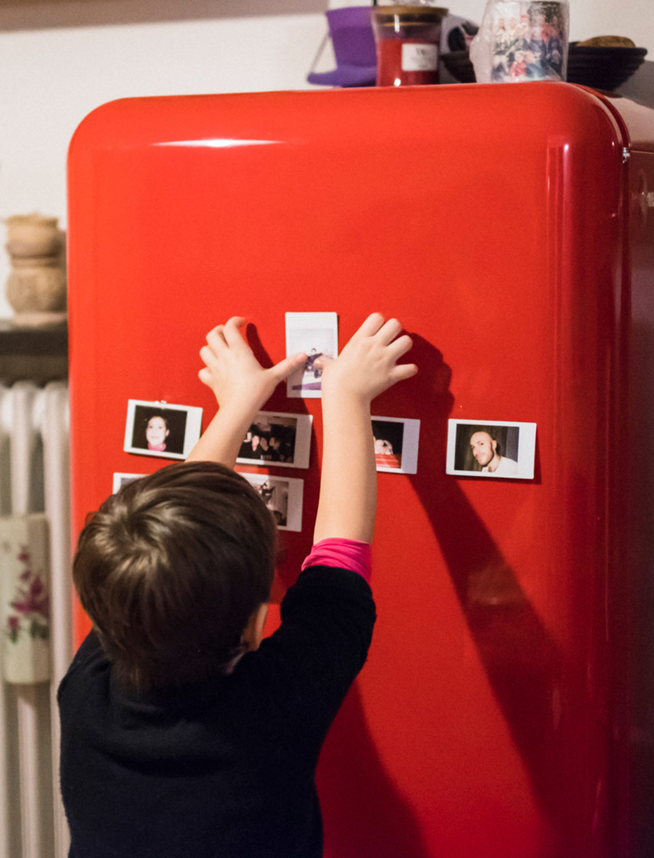 Ein Kind klebt Polaroids an einen roten, pulverlackierten Retro-Kühlschrank